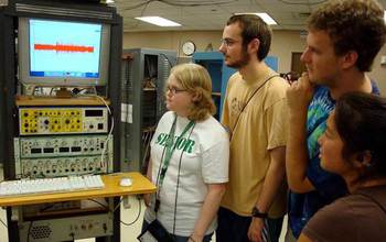 students gathered next to a rack of scientific equipment